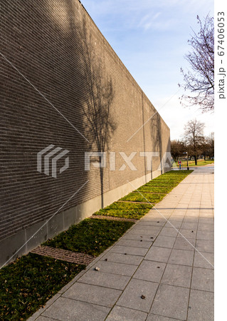 High brick wall with shadows falling on her from the trees, sunny day 67406053