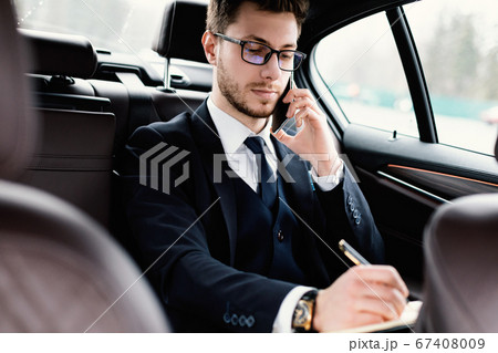 Businessman writing in notebook sitting in his car Businessman writing in notebook sitting in his car 67408009