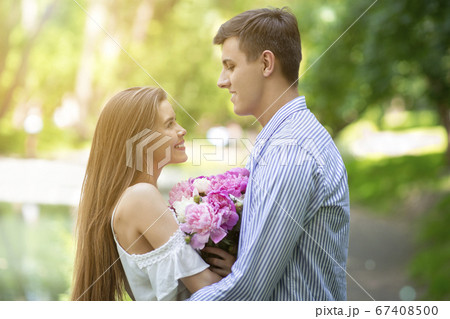 Celebrating anniversary. Loving couple with bouquet of peony flowers at park on summer day Celebrating anniversary. Loving couple with bouquet of peony flowers at park on summer day 67408500