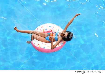 Attractive black woman with glass of summer cocktail on inflatable ring at pool, above view Attractive black woman with glass of summer cocktail on inflatable ring at pool, above view 67408768