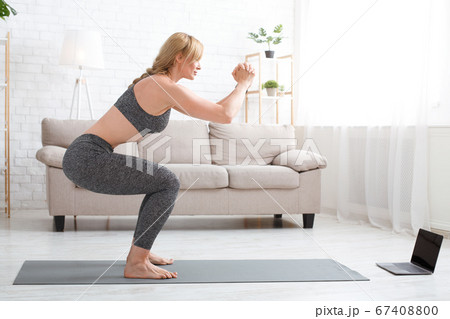 Healthy lifestyle and wellness. Woman in sportswear doing squats, near laptop 67408800