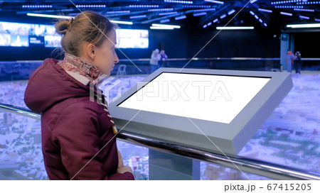 Woman looking at blank white display kiosk at exhibition - white screen concept 67415205