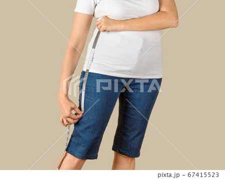 Caucasian mature adult woman measuring a blue denim capris before shortening. Caucasian mature adult woman measuring a blue denim capris before shortening. 67415523