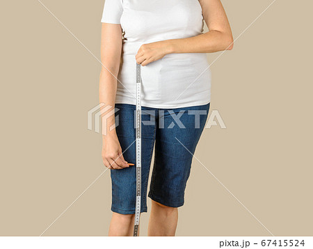 Caucasian mature adult woman drawing a cut line on a blue denim capris before shortening Caucasian mature adult woman drawing a cut line on a blue denim capris before shortening 67415524