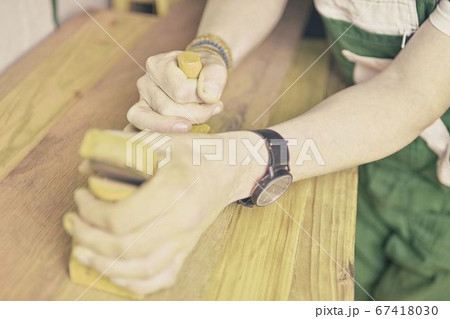 Carpenter working with plane on table in his workshop. Carpenter working with plane in a carpentry shop. Young carpenter wearing bracelets Carpenter working with plane on table in his workshop. Carpenter working with plane in a carpentry shop. Young carpenter wearing bracelets 67418030