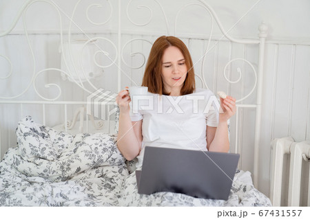 woman drinks tea and eats in bed at computer home. woman drinks tea and eats in bed at computer home. 67431557