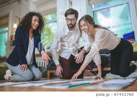 Serious guy and two smiling girls bent over papers 67431760