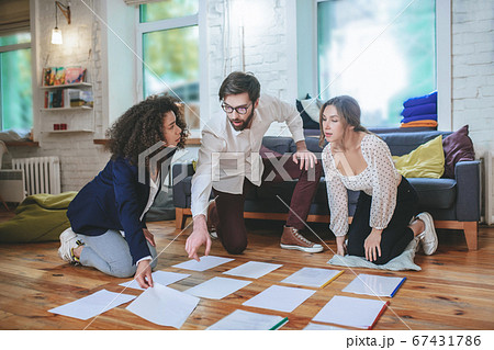 Serious guy with glasses and two girls laying papers on floor 67431786