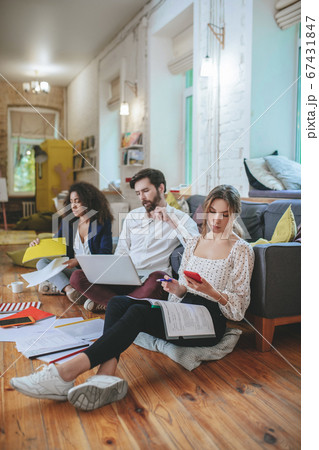 Three young people sitting on the floor in cozy studio working 67431847