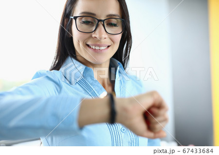 Businesswoman with glasses smiles and looks at her watch Businesswoman with glasses smiles and looks at her watch 67433684