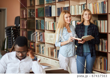 Two young caucasian female students choose books at the library 67437563