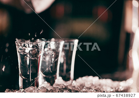Three clean short glasses with vodka stand on ice crumbs on bar stand. Three clean short glasses with vodka stand on ice crumbs on bar stand. 67438927