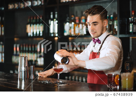 Barman pouring fresh cocktail from shaker into the glass on the bar counter 67438939