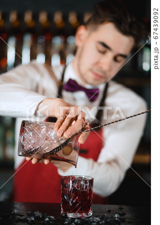 Barman holding a long spoon and glass filled with ice cubes on the bar counter Barman holding a long spoon and glass filled with ice cubes on the bar counter 67439092
