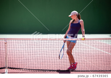 Young woman with tennis racket standing at the net 67439365