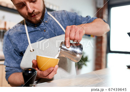 Young barista makes latte in coffee shop Young barista makes latte in coffee shop 67439645