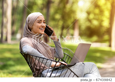 Young muslim woman talking on phone and using laptop 67439842