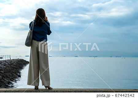 海に向かってスマホで電話する女性の後ろ姿 全身 の写真素材