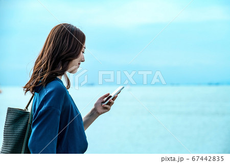 スマホを操作する海に居る若い女性 スマホを操作する海に居る若い女性 67442835