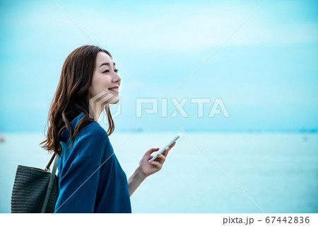 スマホを操作する海に居る若い女性 67442836