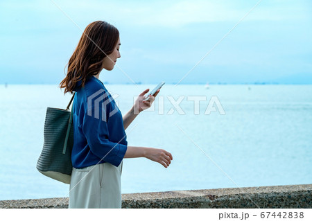 スマホを操作する海に居る若い女性 スマホを操作する海に居る若い女性 67442838