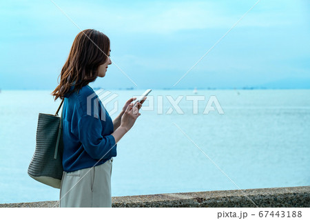 スマホを操作する海に佇む若い女性 67443188