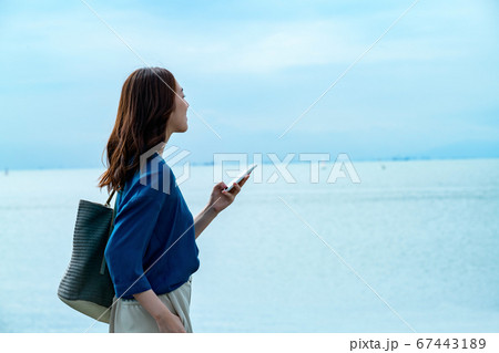 スマホを操作する海に佇む若い女性 67443189