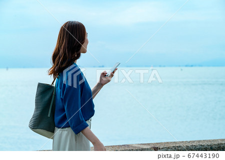 スマホを操作する海に佇む若い女性 67443190