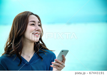 スマホを操作する海に佇む若い女性 67443191