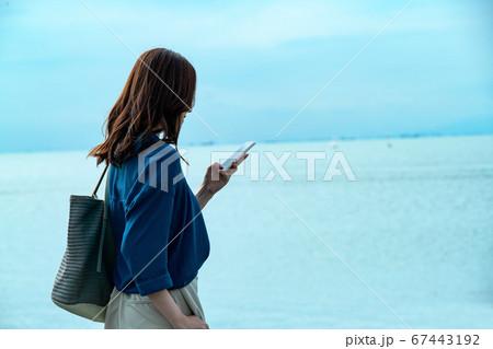 スマホを操作する海に佇む若い女性 67443192