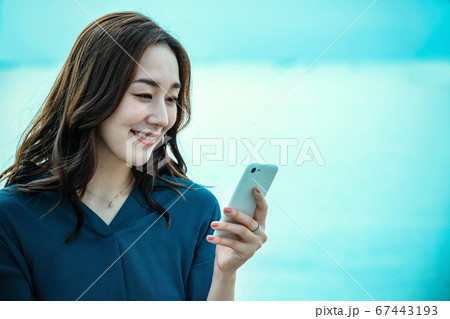 スマホを操作する海に佇む若い女性 67443193