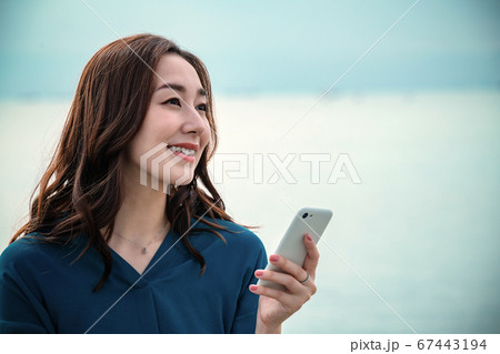スマホを操作する海に佇む若い女性 スマホを操作する海に佇む若い女性 67443194