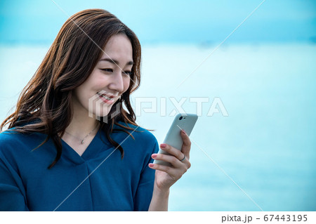スマホを操作する海に佇む若い女性 67443195