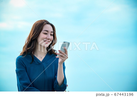 スマホを操作する海に佇む若い女性 67443196