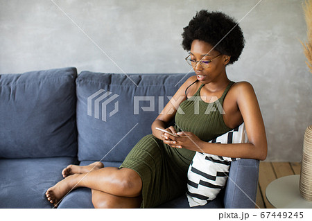 Happy african American young woman sit relax on cozy couch happy to move to new apartment. Smiling black girl rest on comfortable sofa in living room dreaming 67449245