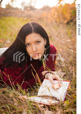 Serious girl in lying in tall grass in the fields with poetry book, she is looking at camera seriously Serious girl in lying in tall grass in the fields with poetry book, she is looking at camera seriously 67449728