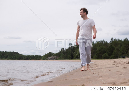 Man walking on the sandy beach looking on water Man walking on the sandy beach looking on water 67450456