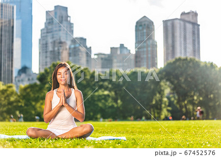 New York City Central Park yoga girl relaxing meditating woman in meditation in outside in summer. Beautiful young mixed race Asian Caucasian model sitting in lotus pose in grass New York City Central Park yoga girl relaxing meditating woman in meditation in outside in summer. Beautiful young mixed race Asian Caucasian model sitting in lotus pose in grass 67452576