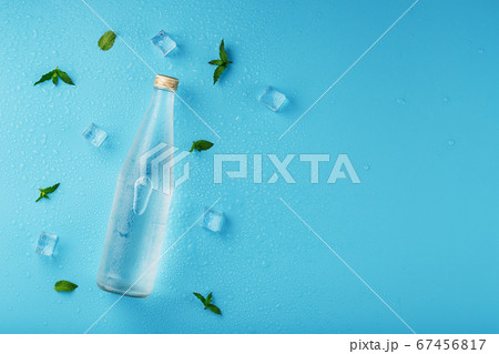 A bottle of ice water, ice cubes, drops and mint 67456817