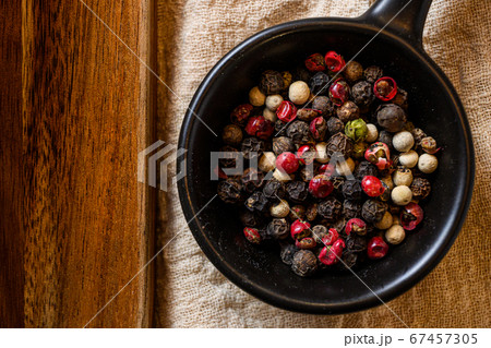 Mix of peppercorns in black bowl on linen cloth 67457305