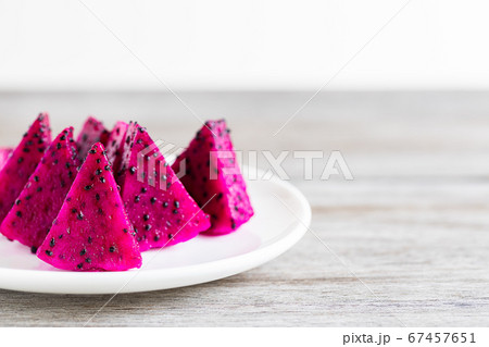 Sliced pink dragon fruit on white ceramic plate on wooden table, selective focus Sliced pink dragon fruit on white ceramic plate on wooden table, selective focus 67457651