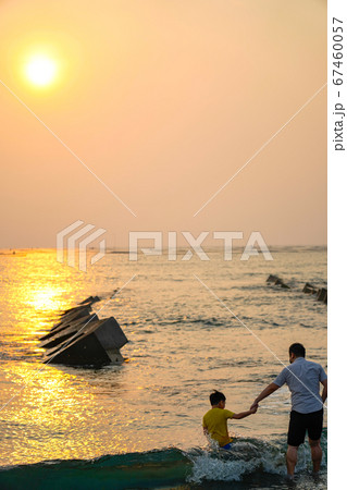 View from the beach with a yellow glowing sun setting in the horizon with an Asian family playing in the water. View from the beach with a yellow glowing sun setting in the horizon with an Asian family playing in the water. 67460057