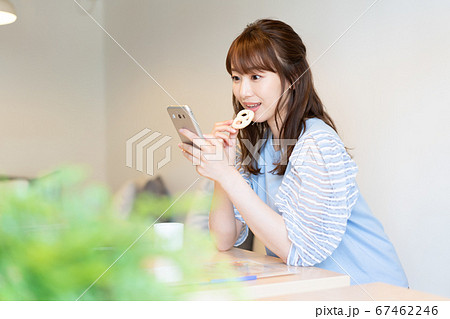 カフェでクッキーをかじりながらスマホを見る若い女性 67462246