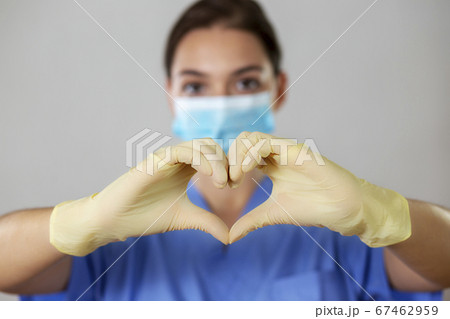 Female nurse in a face mask makes the heart shape with her fingers in gloves. 67462959