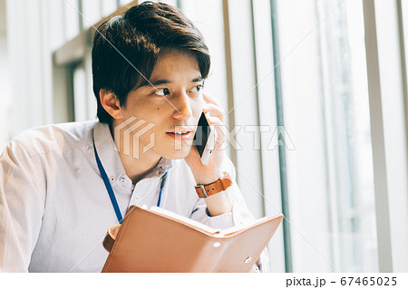 手帳を持って電話をする若い男性 67465025