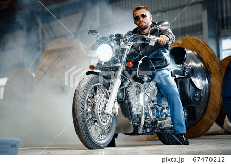 Bearded motorcyclist in black leather clothing with his motorbike Bearded motorcyclist in black leather clothing with his motorbike 67470212