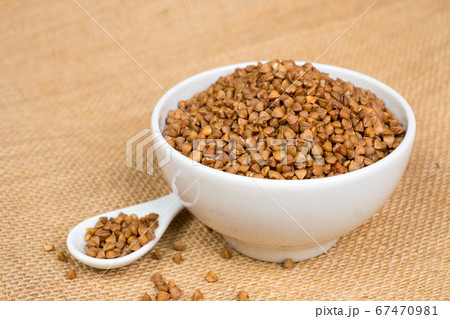 dry buckwheat heap in white bowl with spoon over dry buckwheat heap in white bowl with spoon over 67470981
