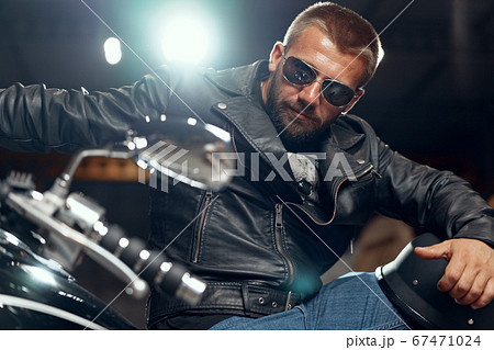 Portrait of bearded man motocyclist in dark sunglasses on dark background 67471024