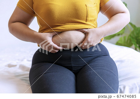 Overweight young woman pinches fat on her belly Overweight young woman pinches fat on her belly 67474085