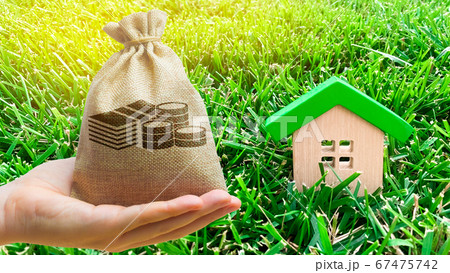 Miniature wooden house and money bag on grass. Real estate concept. Eco-friendly and energy efficient house. Buying a home outside the city. The urban downshift. Nature. Fresh air. Mortgage, loan. 67475742
